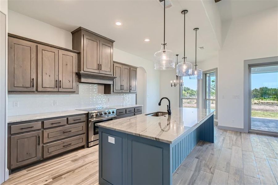 Kitchen with decorative backsplash, a kitchen island with sink, stainless steel range, and light hardwood / wood-style flooring