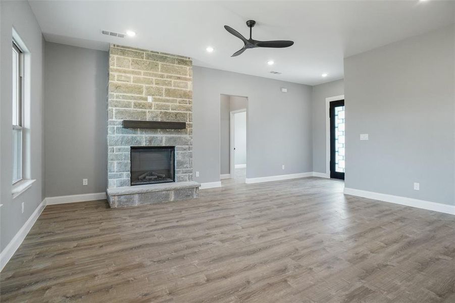 Unfurnished living room with a stone fireplace, ceiling fan, and hardwood / wood-style floors