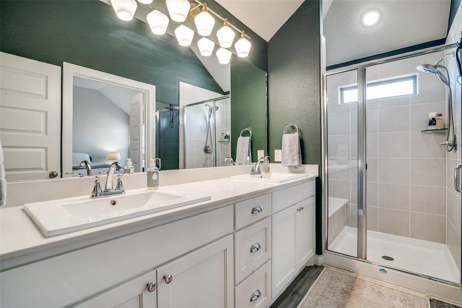 Bathroom featuring vanity, hardwood / wood-style floors, vaulted ceiling, and a shower with door