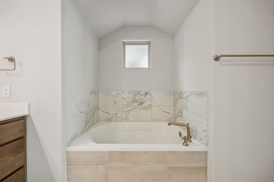 Bathroom featuring lofted ceiling, vanity, and tiled bath