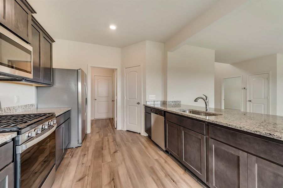 Kitchen with appliances with stainless steel finishes, sink, light stone counters, and light hardwood / wood-style flooring