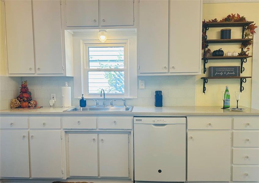 Kitchen with white cabinetry, decorative backsplash, dishwasher, and sink