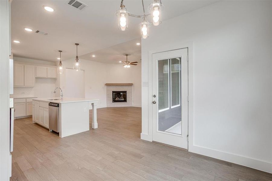 Kitchen with hanging light fixtures, light wood-type flooring, stainless steel dishwasher, an island with sink, and a tile fireplace