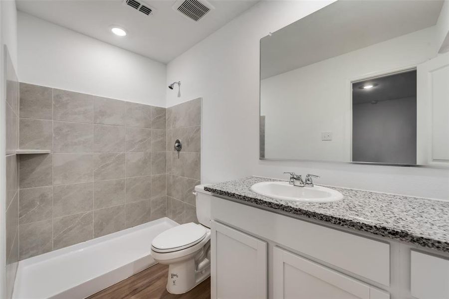 Bathroom featuring tiled shower, hardwood / wood-style floors, toilet, and vanity