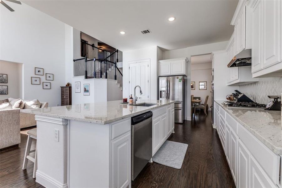 Kitchen featuring granite counters, vent hood, an island with sink and white cabinets