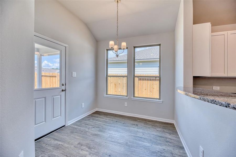 The breakfast room offers large windows that bathe the space in natural light, complemented by a suspended chandelier for added elegance. A door leads to the backyard covered patio, extending the dining experience outdoors and providing a perfect spot for enjoying meals al fresco.