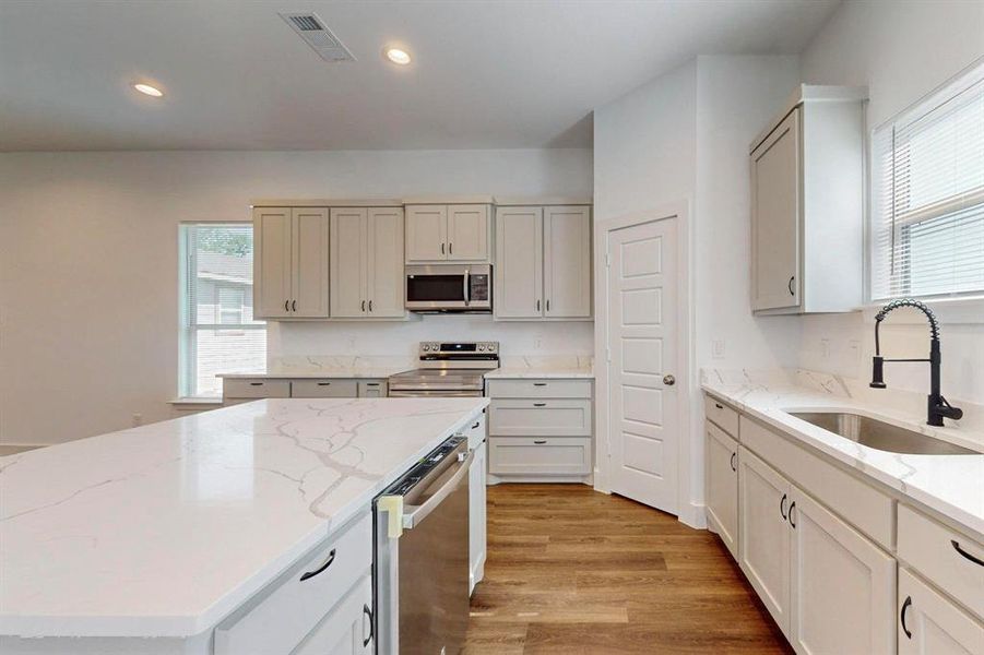 Kitchen featuring stainless steel appliances, light stone countertops, a center island, light wood-type flooring, and sink