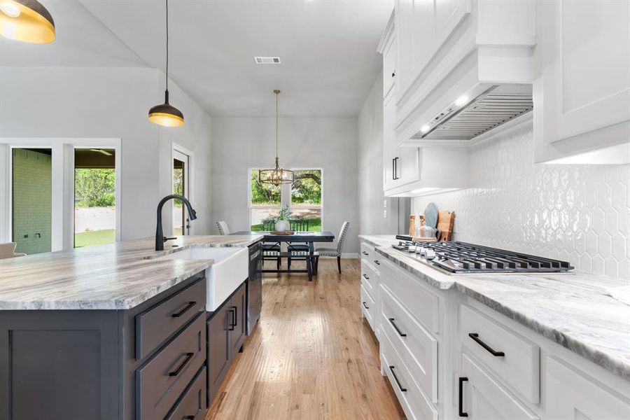 Kitchen with decorative light fixtures, light hardwood / wood-style floors, tasteful backsplash, custom exhaust hood, and white cabinets