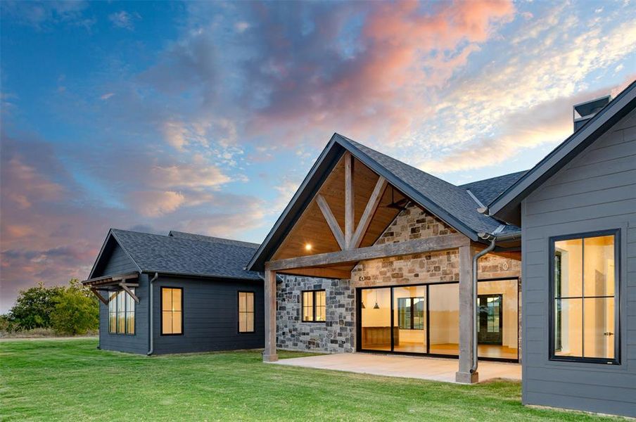 Back house at dusk featuring a patio area and a lawn