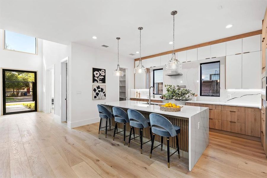 Kitchen with light hardwood / wood-style floors, white cabinetry, decorative light fixtures, a kitchen island with sink, and sink