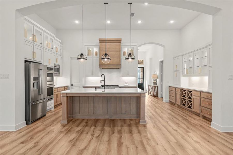 Kitchen with appliances with stainless steel finishes, white cabinets, light wood-type flooring, and a kitchen island with sink
