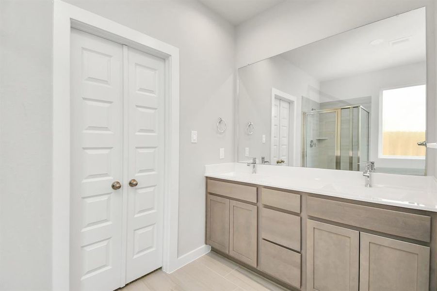 The primary bathroom is located alongside a spacious walk-in closet with shelving, high ceilings, custom paint, and sleek, dark modern finishes. An ideal retreat for unwinding after a long day! Sample photo of completed home with similar floor plan. Actual colors and selections may vary.