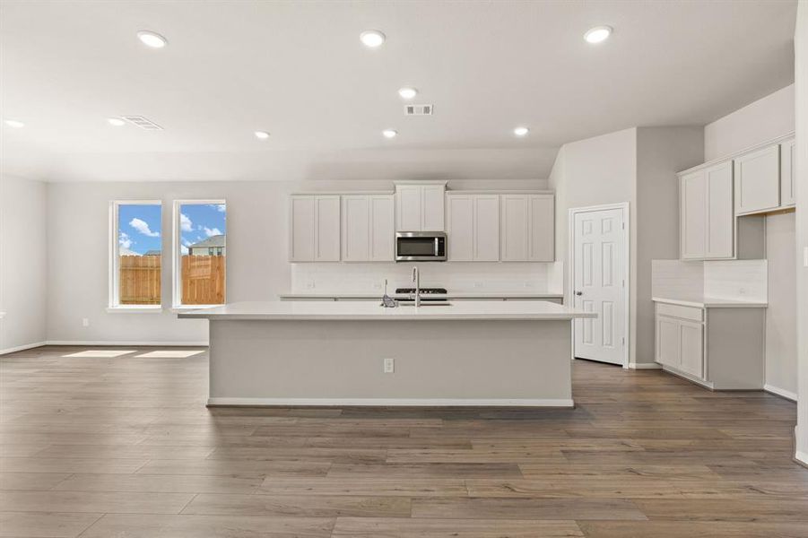 This light and bright kitchen features a large quartz island, white cabinets, a large sink overlooking your family room, recessed lighting, and beautiful backsplash.