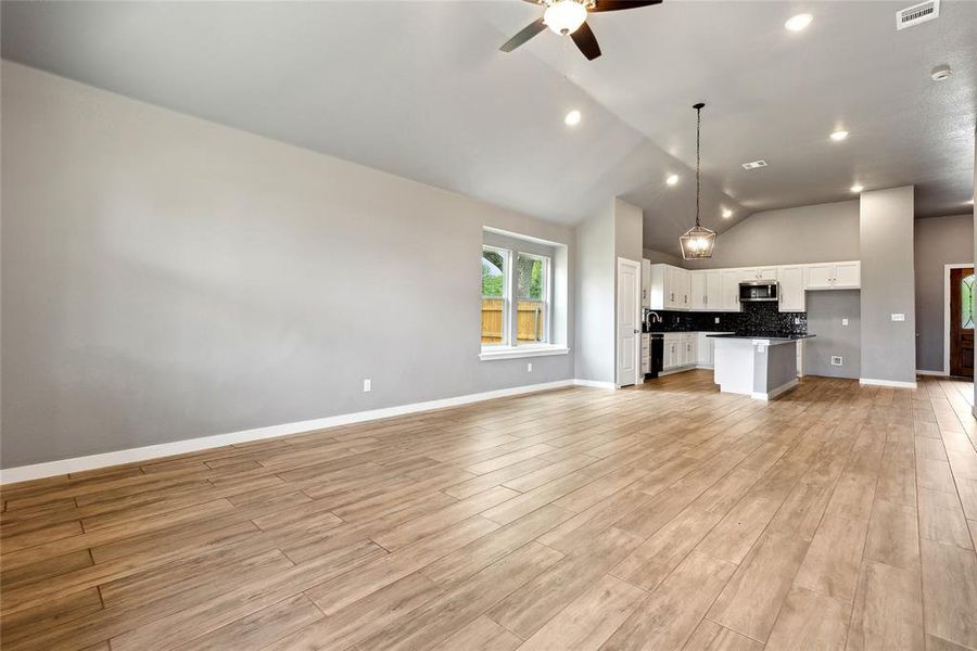 Unfurnished living room with light wood-type flooring, ceiling fan, and high vaulted ceiling