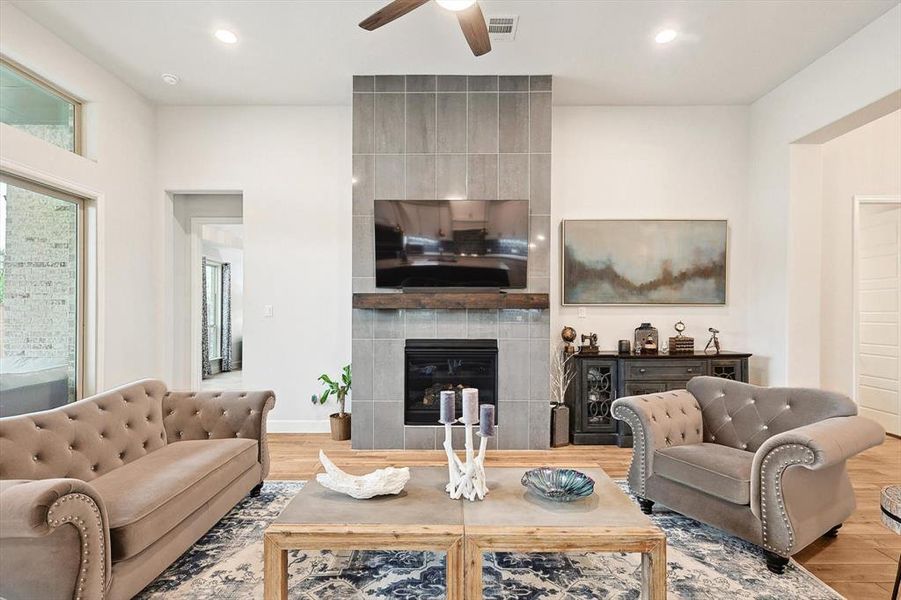 Living room featuring ceiling fan, a tiled fireplace, and light wood-type flooring