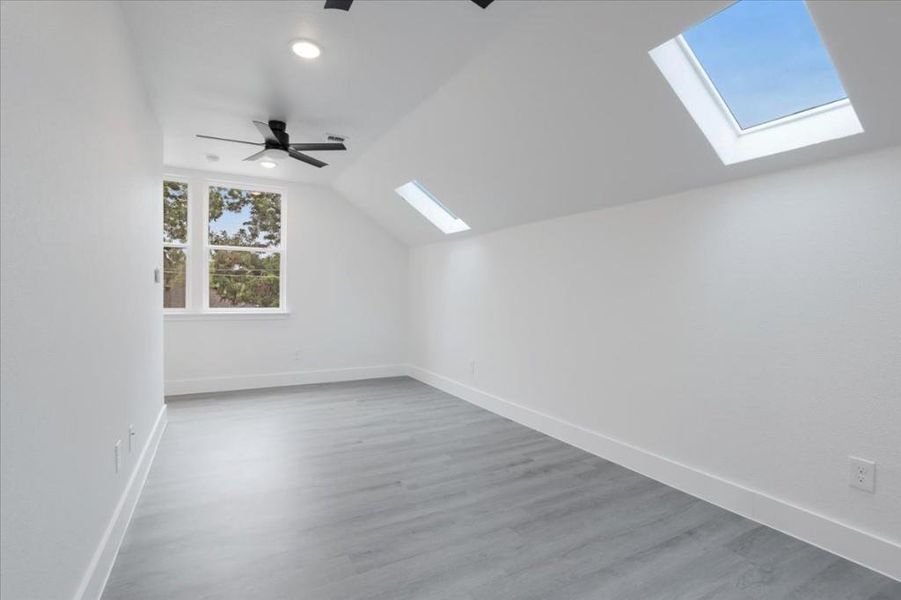 Bonus room with lofted ceiling with skylight, wood-type flooring, and ceiling fan