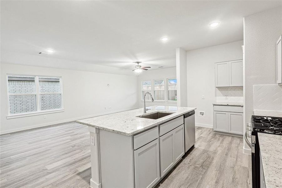 Kitchen with stainless steel appliances, sink, a kitchen island with sink, light wood-type flooring, and ceiling fan