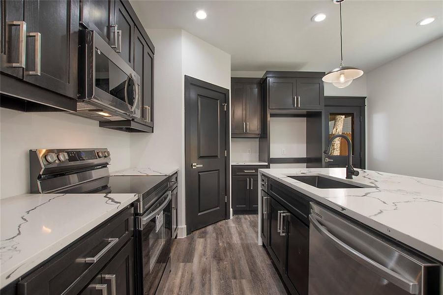 Kitchen featuring sink, appliances with stainless steel finishes, dark wood-type flooring, light stone counters, and hanging light fixtures