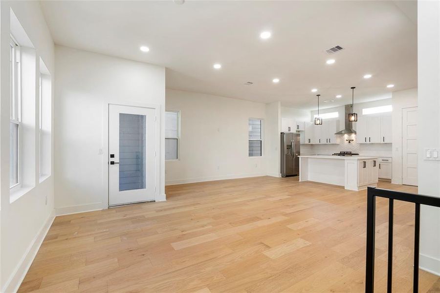 This is a bright, open-concept living space featuring a modern kitchen with stainless steel appliances and a center island, recessed lighting, hardwood floors, and large windows providing ample natural light. The space is versatile for dining and living arrangements with a neutral color palette, perfect for personal customization.