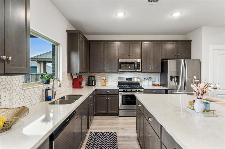 Kitchen with decorative backsplash, dark brown cabinets, appliances with stainless steel finishes, light wood-type flooring, and sink