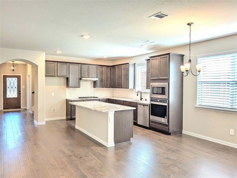 Kitchen with an inviting chandelier, decorative light fixtures, stainless steel appliances, and dark hardwood / wood-style floors