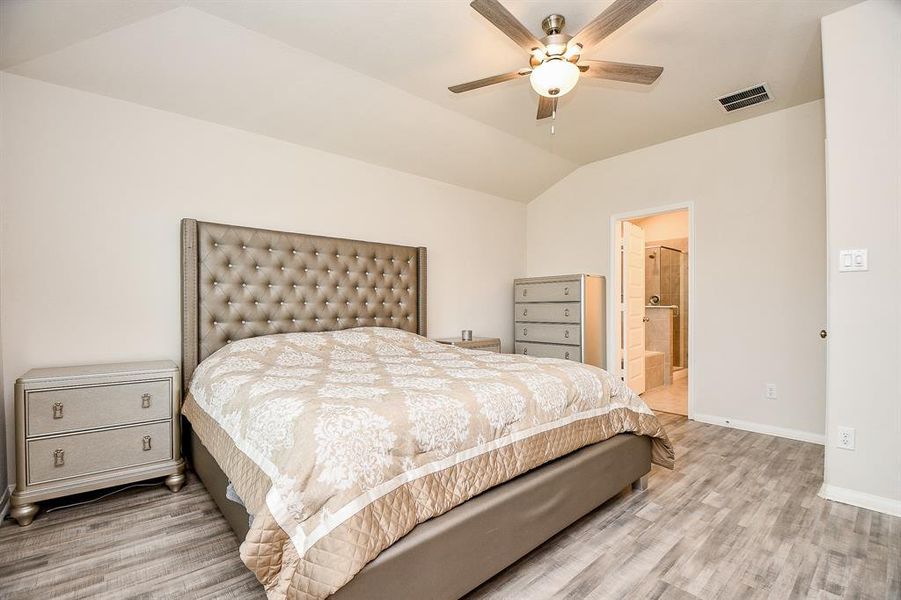 Spacious primary bedroom with a vaulted ceiling and ceiling fan. It features contemporary styling, laminate flooring, and neutral colors. There's direct access to an en suite bathroom.