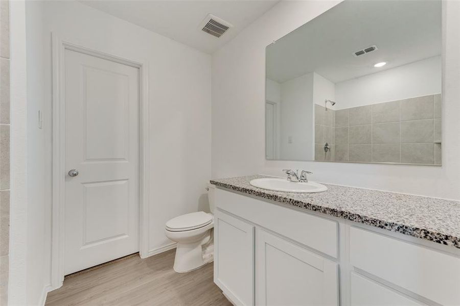 Bathroom featuring vanity, tiled shower, toilet, and hardwood / wood-style flooring