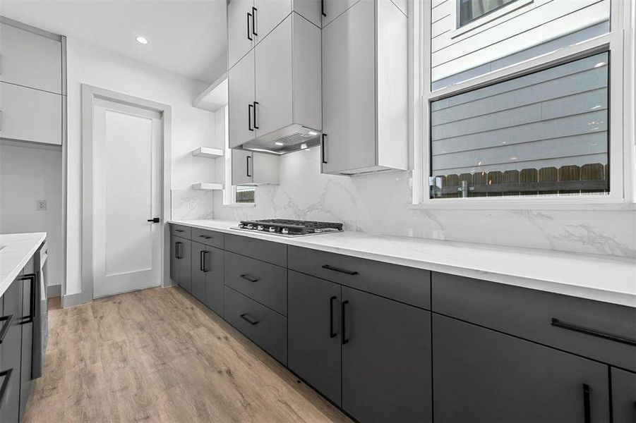 Kitchen featuring gray cabinets, white cabinets, stainless steel gas stovetop, light wood-type flooring, and backsplash