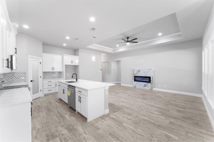 Kitchen with white cabinetry, a center island with sink, a tray ceiling, and sink