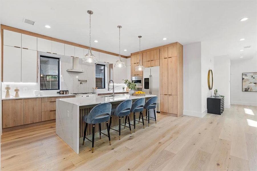 Kitchen featuring light hardwood / wood-style floors, a kitchen island with sink, white cabinetry, hanging light fixtures, and stainless steel fridge