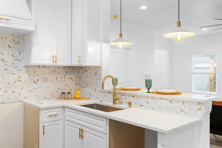 Kitchen featuring wood-type flooring, hanging light fixtures, kitchen peninsula, sink, and white cabinets