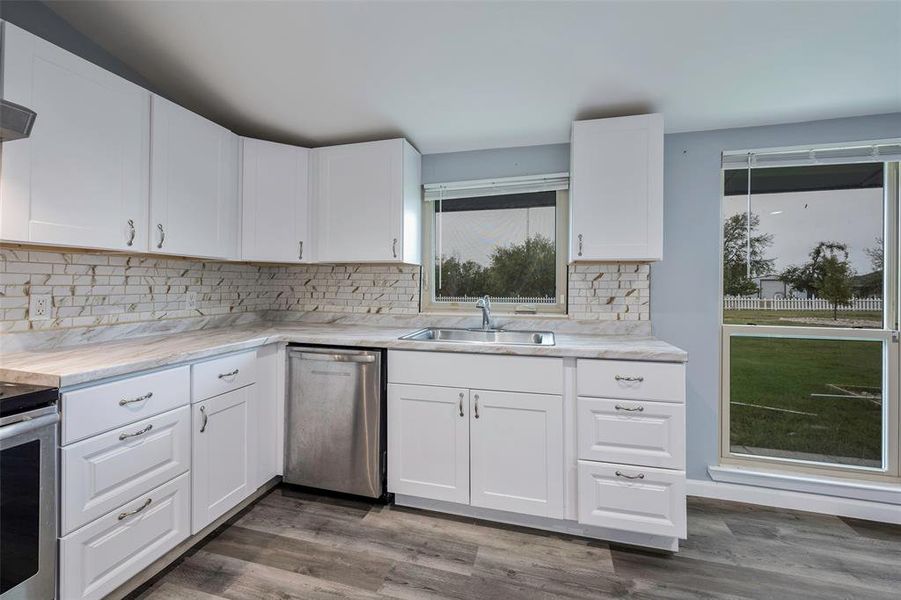 Kitchen with stainless steel appliances, sink, backsplash, hardwood / wood-style floors, and white cabinets