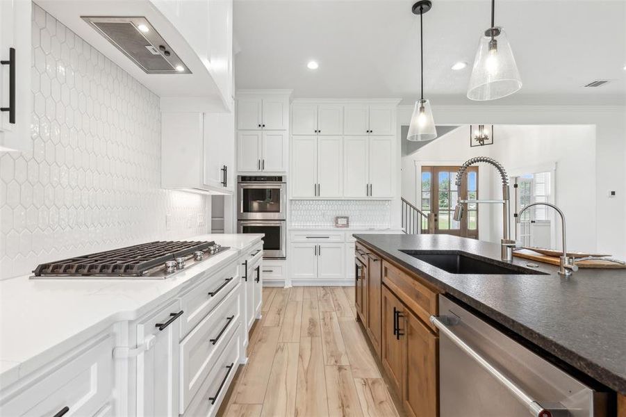 Kitchen with light hardwood / wood-style floors, stainless steel appliances, white cabinets, sink, and tasteful backsplash