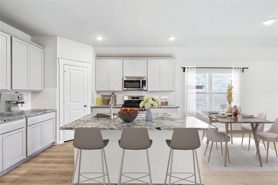 Kitchen featuring appliances with stainless steel finishes, light stone countertops, light wood-type flooring, and an island with sink