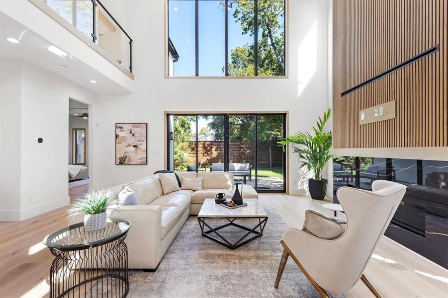 Living room with a healthy amount of sunlight, a towering ceiling, and light hardwood / wood-style flooring