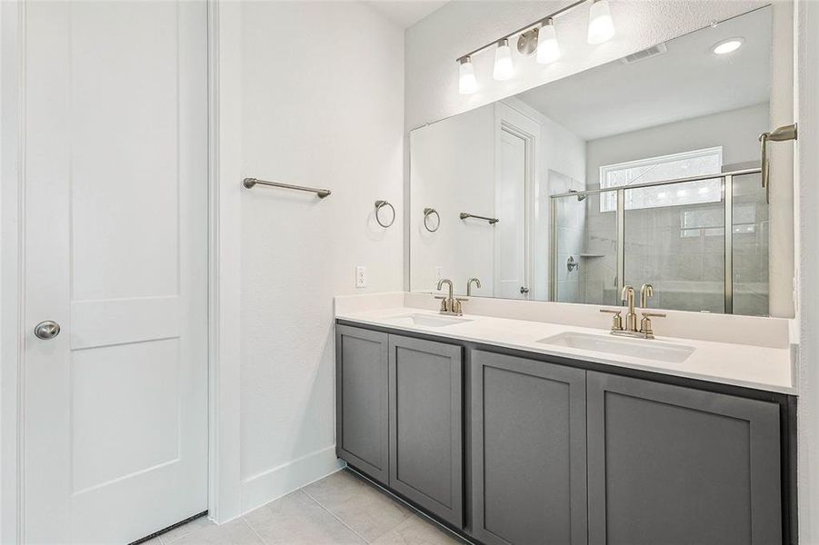 Bathroom featuring tile patterned flooring, double vanity, and a shower with door