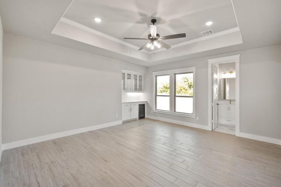 Unfurnished living room featuring light hardwood / wood-style floors, a raised ceiling, ornamental molding, and ceiling fan