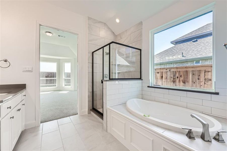 Bathroom with tile flooring, separate shower and tub, lofted ceiling, and vanity