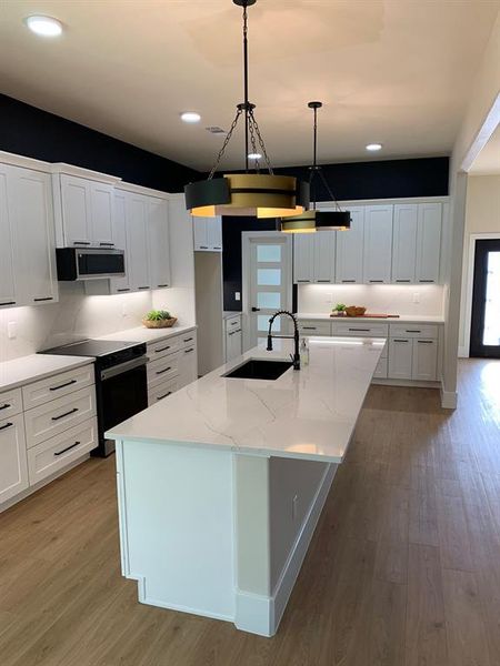 Kitchen featuring range with electric cooktop, sink, light wood-type flooring, white cabinetry, and a center island with sink