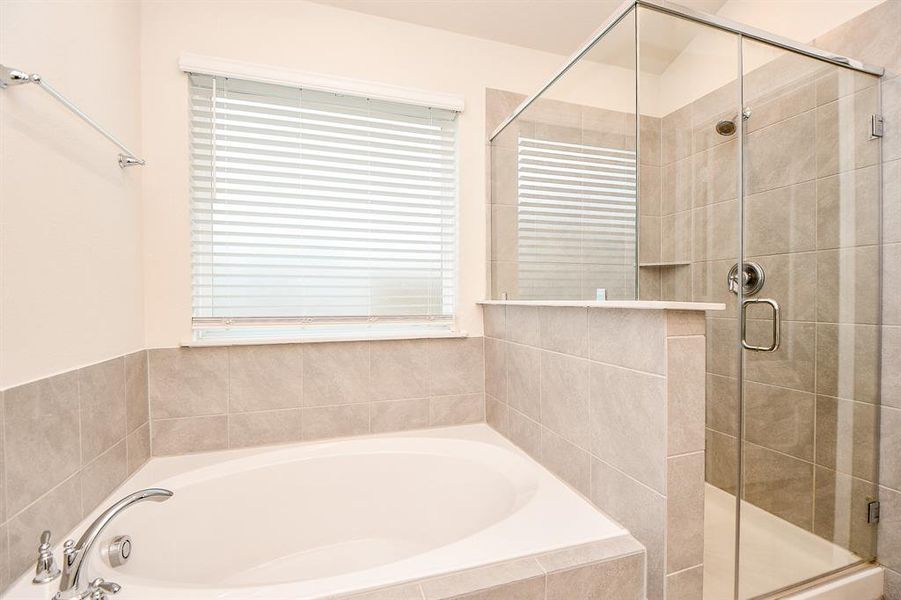 This is a modern bathroom featuring a large corner soaking tub and a separate glass-enclosed shower, with neutral tile surrounds.