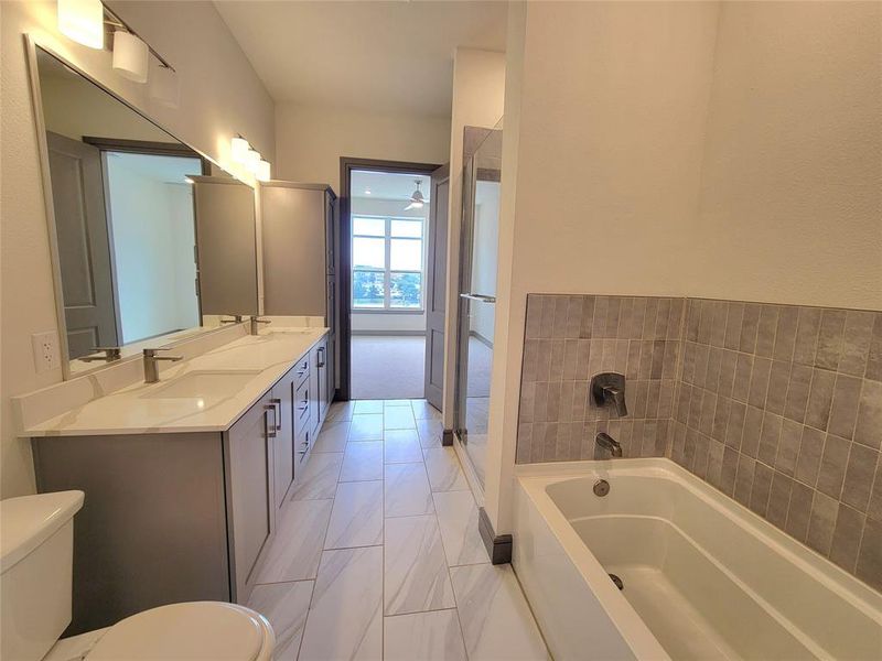 Bathroom featuring tile floors, dual bowl vanity, toilet, and a tub