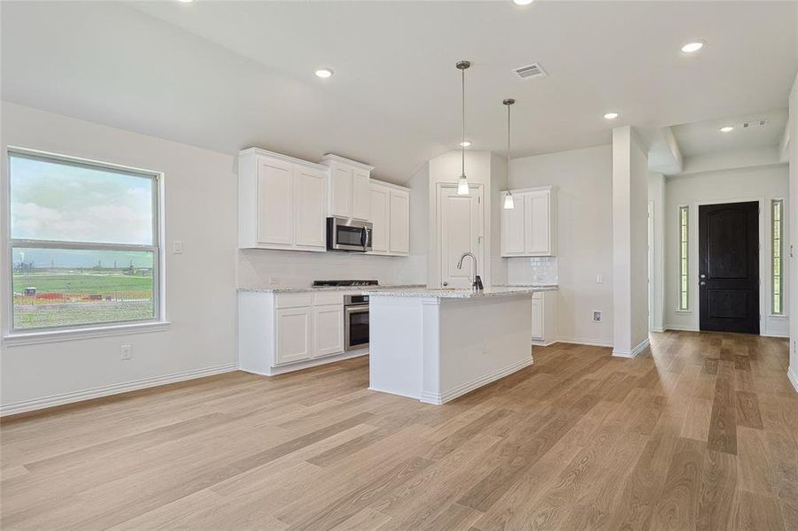 Kitchen with light stone countertops, stainless steel appliances, white cabinets, and light hardwood / wood-style floors