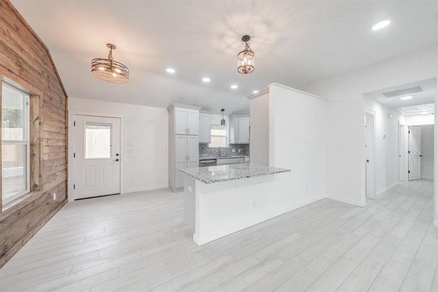 Kitchen with light stone counters, wood walls, kitchen peninsula, an inviting chandelier, and decorative light fixtures