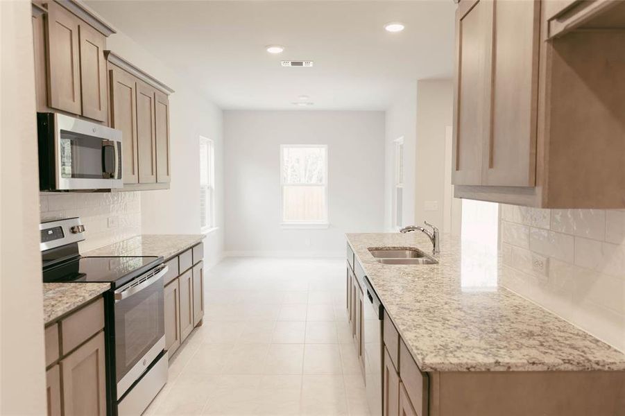 Kitchen featuring stainless steel appliances, sink, light stone counters, light tile patterned floors, and decorative backsplash