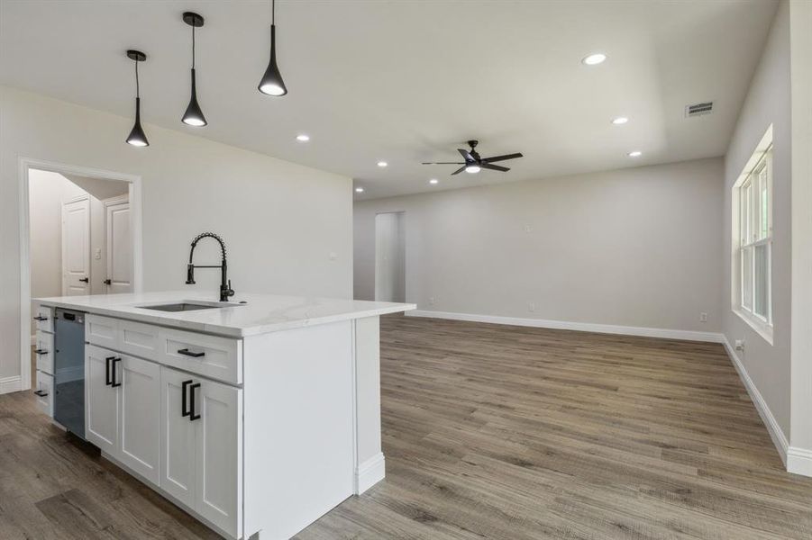 Kitchen with sink, an island with sink, white cabinets, decorative light fixtures, and ceiling fan