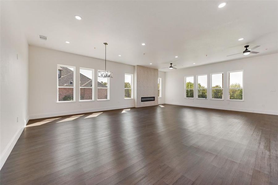 Unfurnished living room with ceiling fan with notable chandelier, dark hardwood / wood-style flooring, and a large fireplace