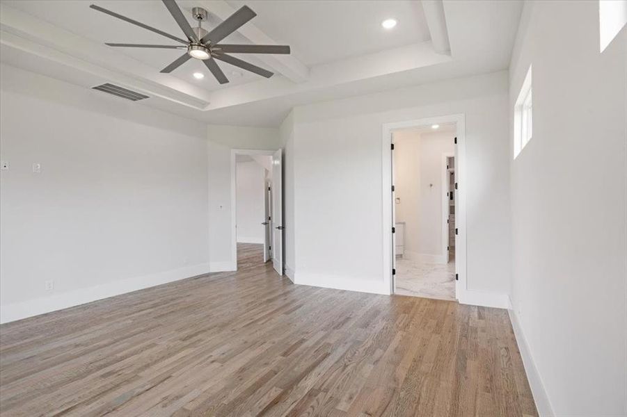 Unfurnished bedroom featuring a tray ceiling, ceiling fan, light hardwood / wood-style floors, and connected bathroom
