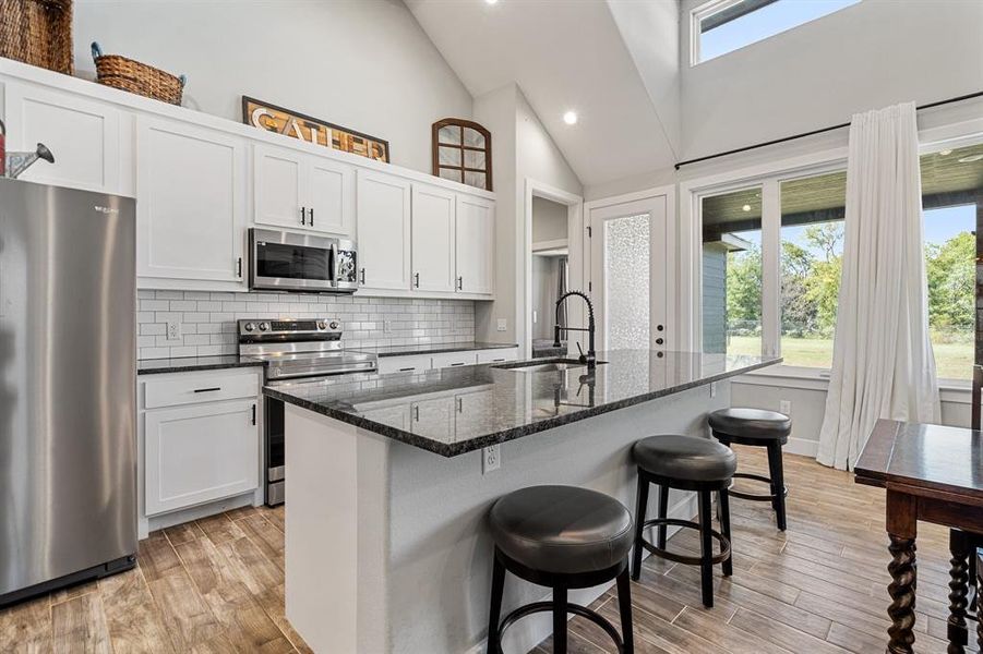 Kitchen with a kitchen island with sink, white cabinetry, light hardwood / wood-style flooring, and appliances with stainless steel finishes