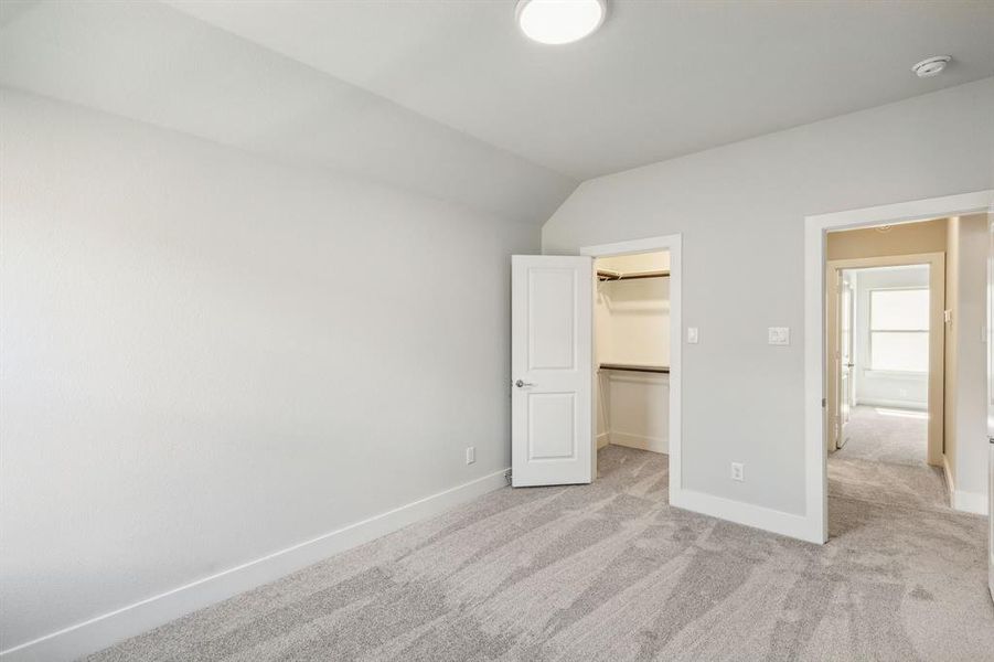 Unfurnished bedroom with vaulted ceiling, a walk in closet, light colored carpet, and a closet