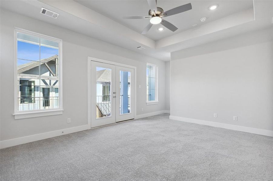 Carpeted spare room featuring ceiling fan, french doors, and a raised ceiling